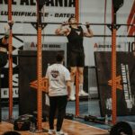 Athletes performing pull-ups in a CrossFit competition, judged by officials, showcasing strength and endurance.